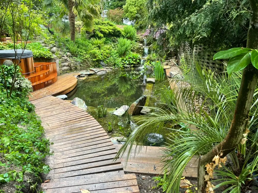 Lush garden pond with wooden deck and hot tub