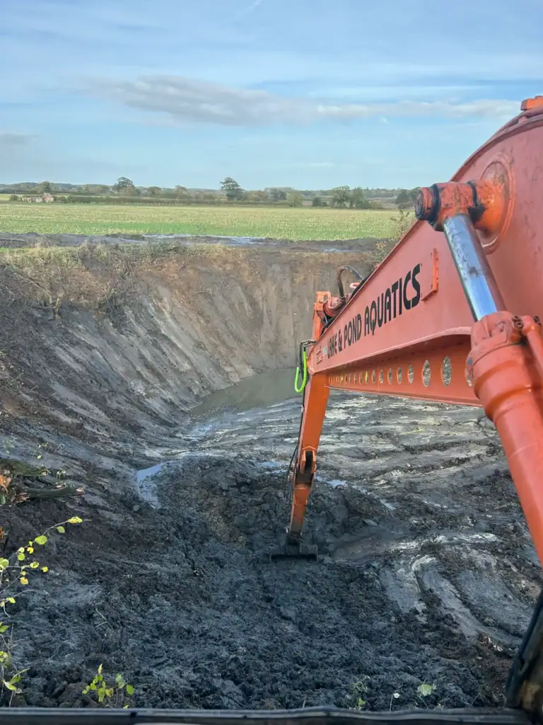 Excavator digging large pond in rural field