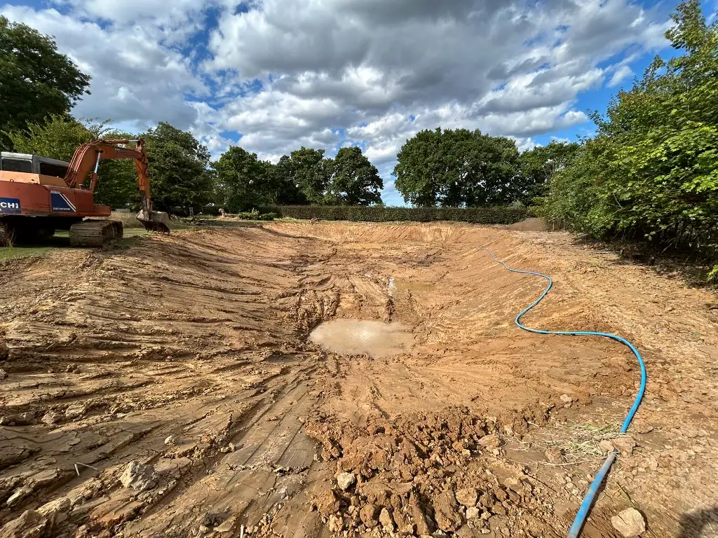 Excavator digging large pond in muddy field