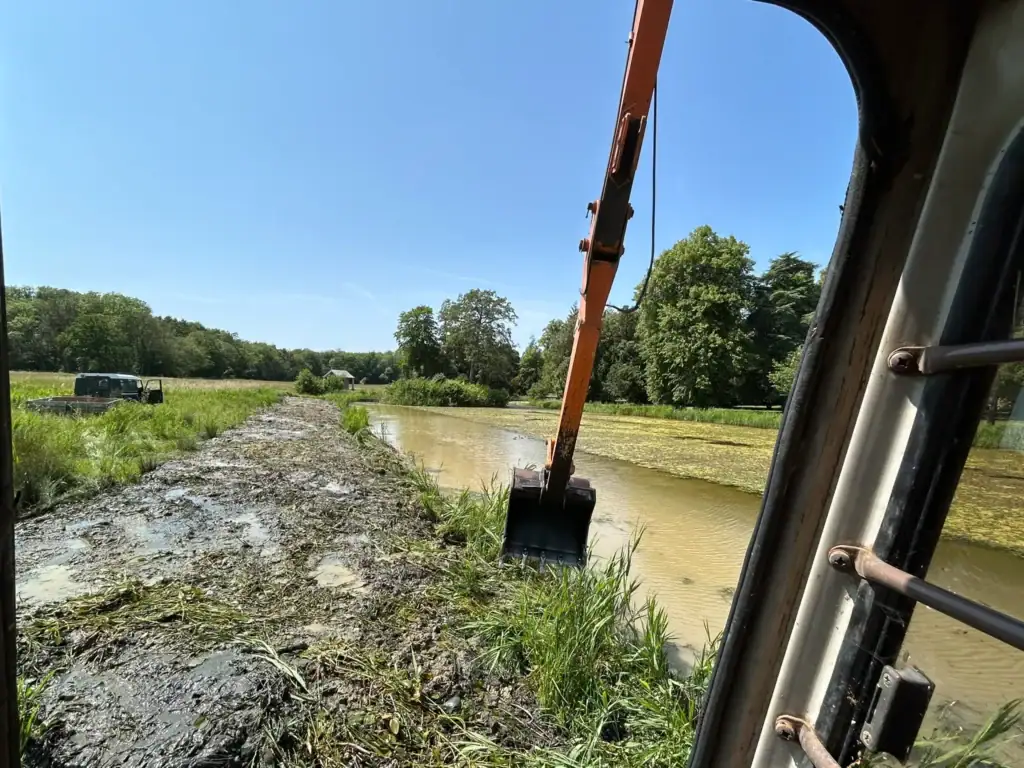 Excavator dredging muddy pond in rural landscape