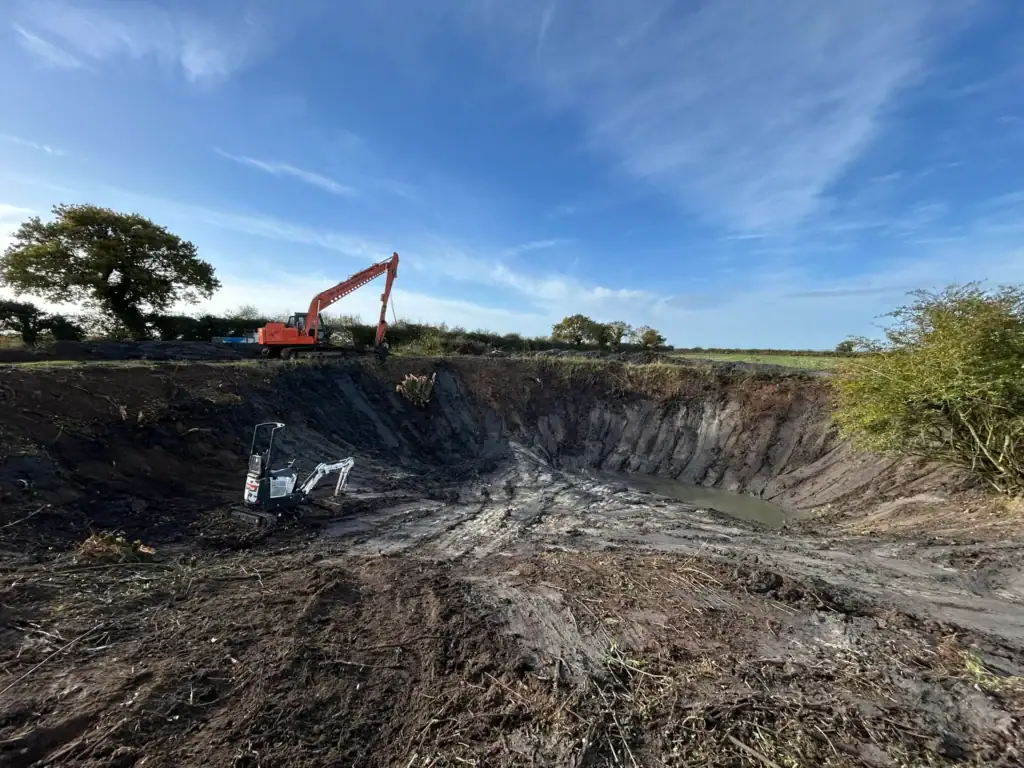 Excavators digging large pond in countryside
