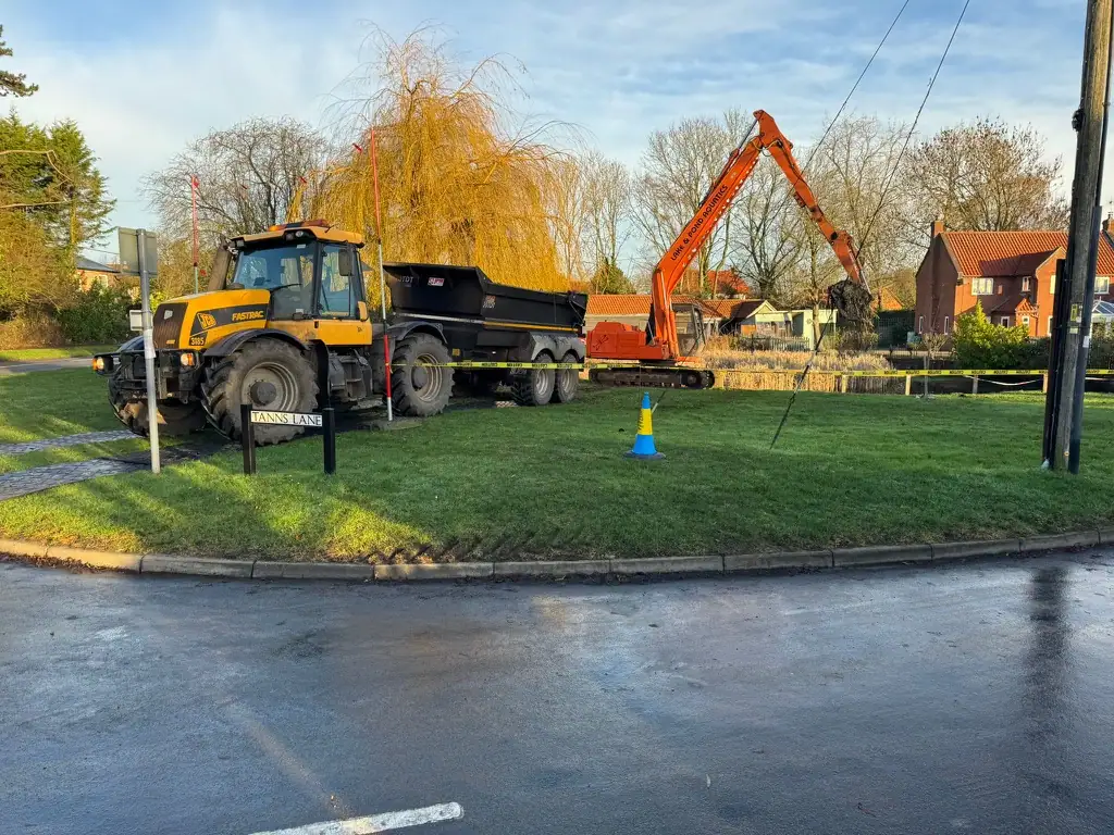 Tractor and excavator on grassy roadside verge
