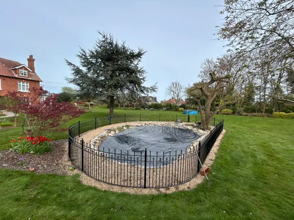 Fenced covered garden pond in large lawn