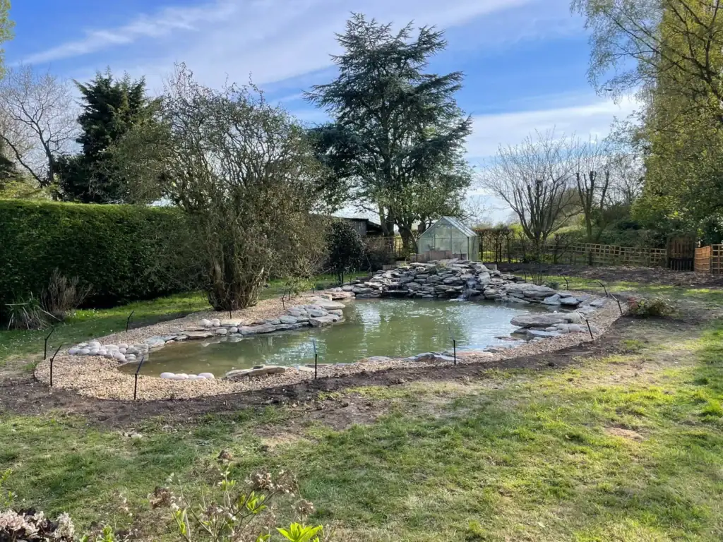 Landscaped garden pond with rock waterfall and greenhouse