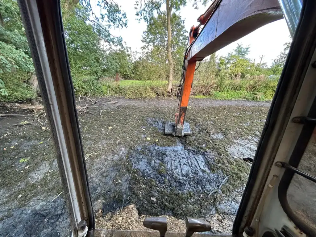 Excavator digging muddy riverbank from cab view
